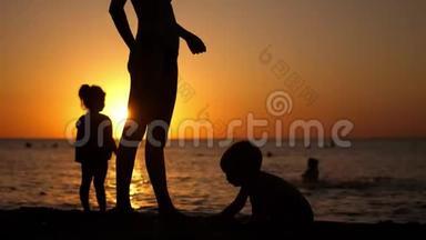 幸福的家庭母亲带着孩子在日落时在海滩度假。